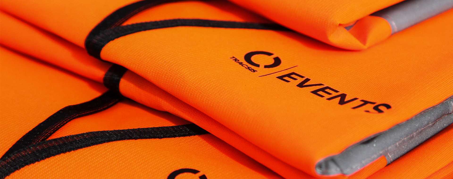 A stack of orange Tracsis Events branded high visibility jackets
